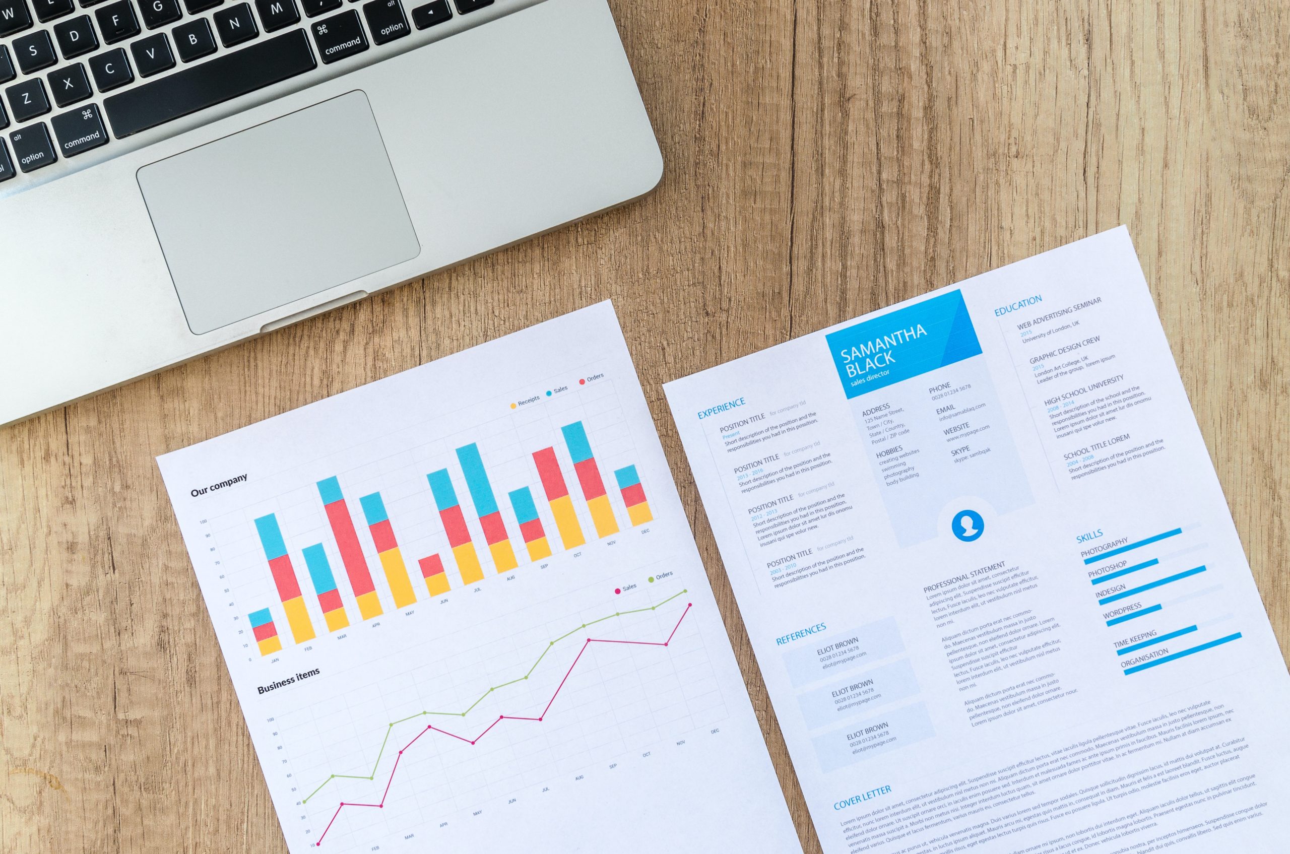 There is a resume and a business analytics report kept on a table in front of a laptop